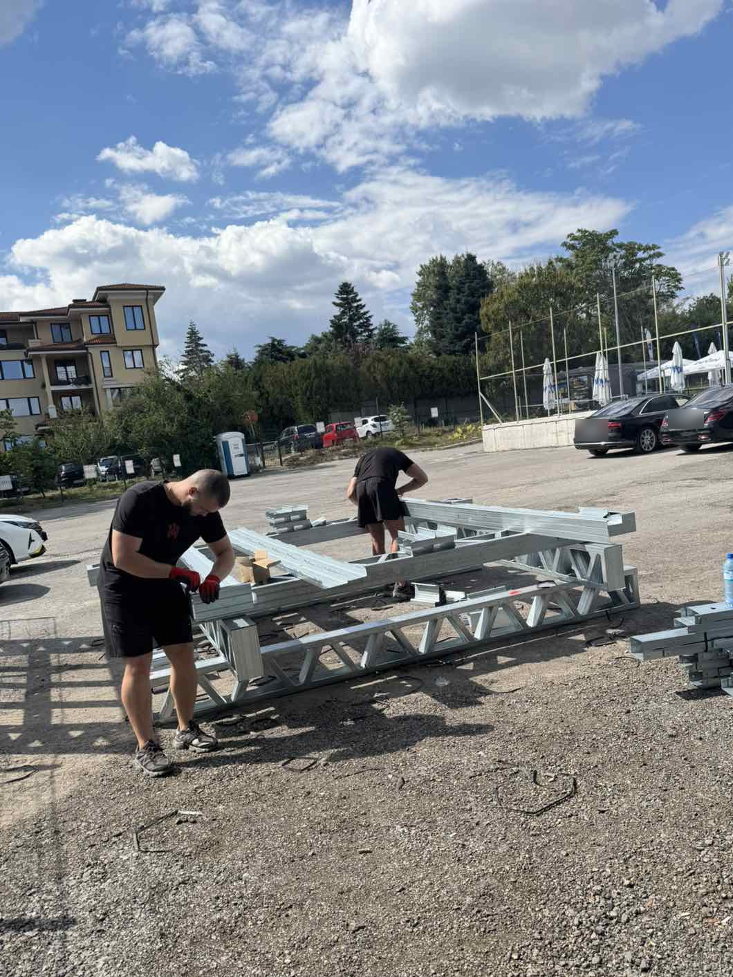 Два монтажника собирают элемент из оцинкованных профилей на площадке